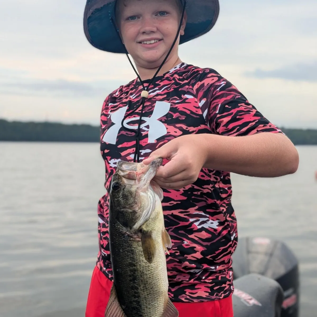 A young angler in a sun hat with a largemouth bass on the deck
