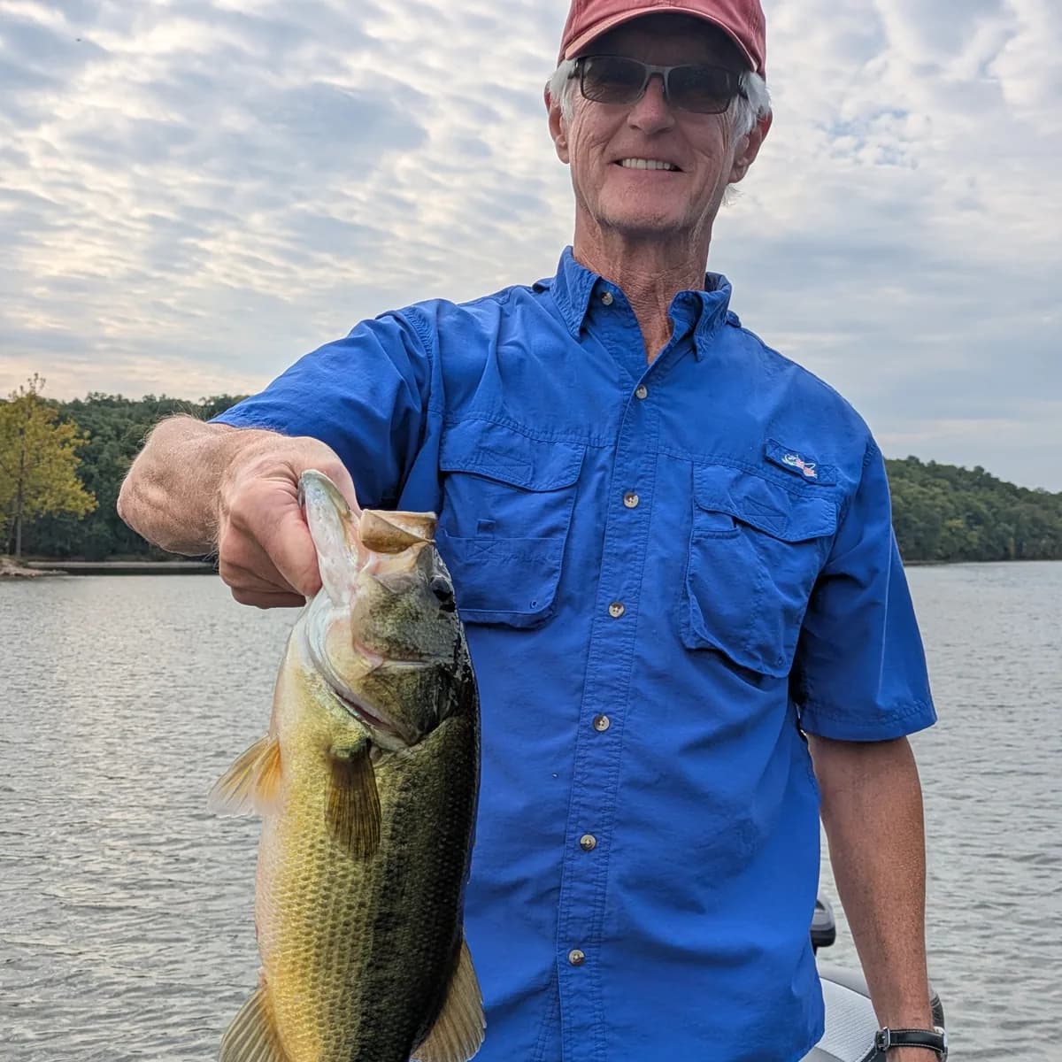 An angler in a blue fishing shirt with a largemouth bass in the evening light