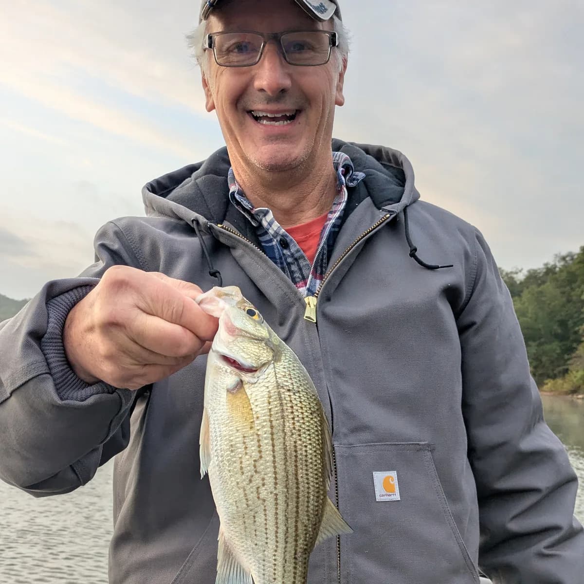 An angler in a grey work jacket holding a white bass on a September morning