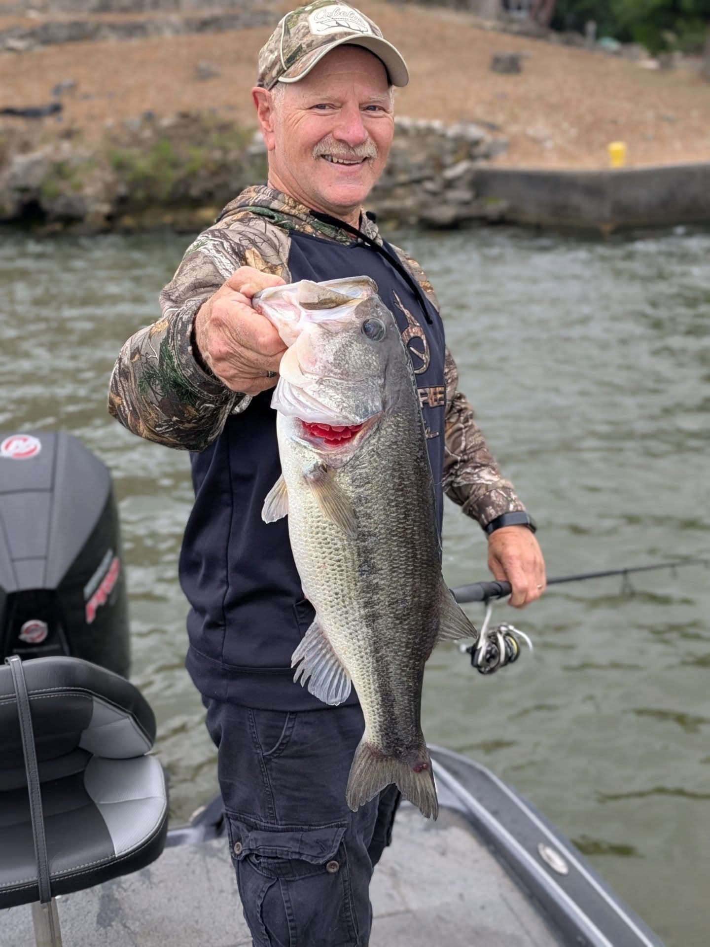 An angler in camo holding out a big largemouth bass on Lake of the Ozarks